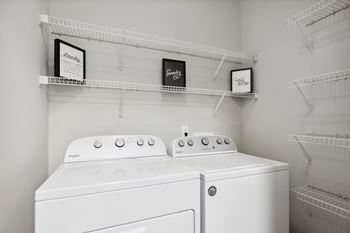 Two white washing machines in a laundry room with shelves above them.